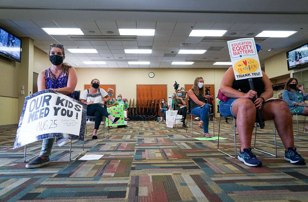 Protesters with boards sit at the back of the Columbia School Board meeting